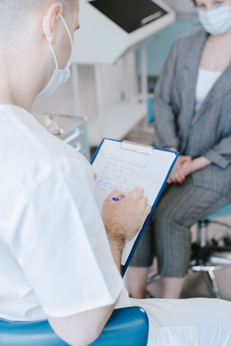 A medical professional takes notes while consulting with a patient in a clinical setting.